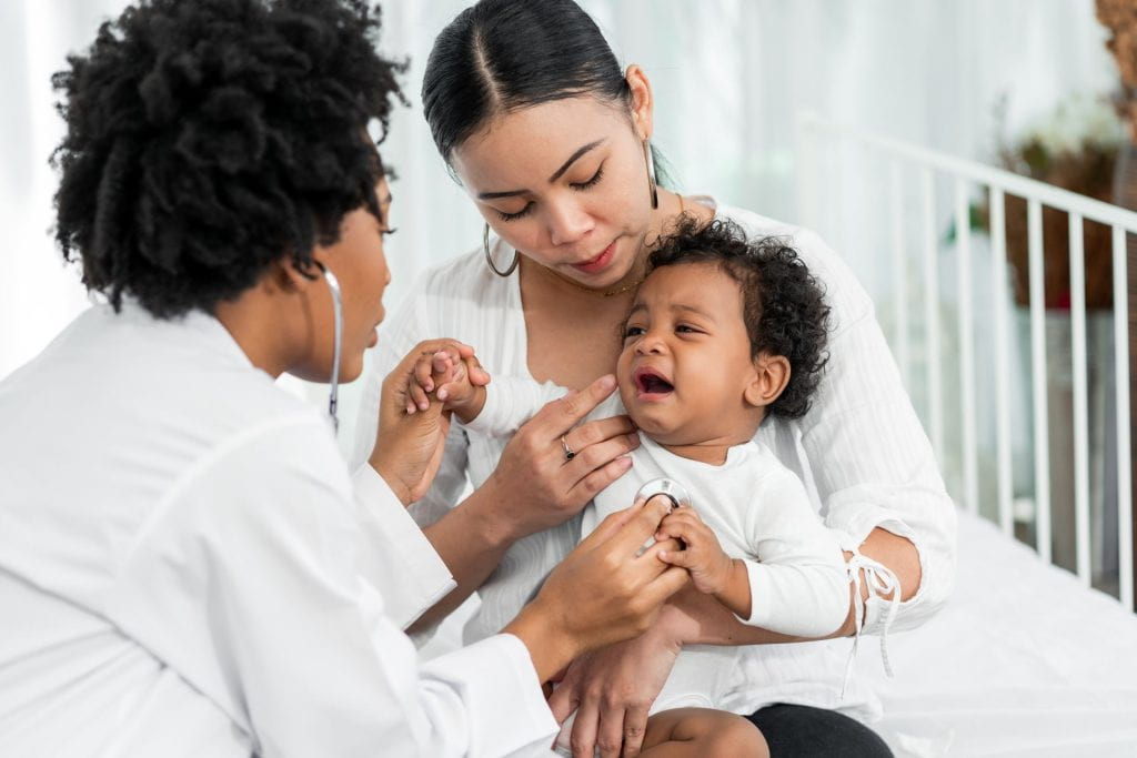 Black female pediatrician hold stethoscope exam child boy patient visit doctor with mother (stock photo)